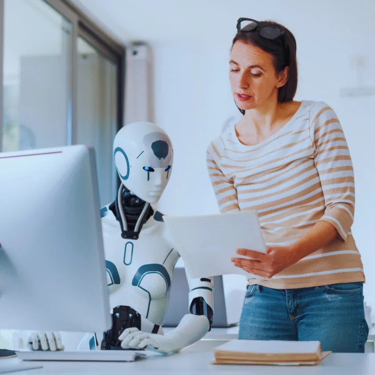 An HR professional reviews a document while an AI assistant works at the computer